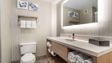 Un baño moderno con inodoro, lavabo y espejo. Hay toallas en estantes y un perchero sobre el inodoro.