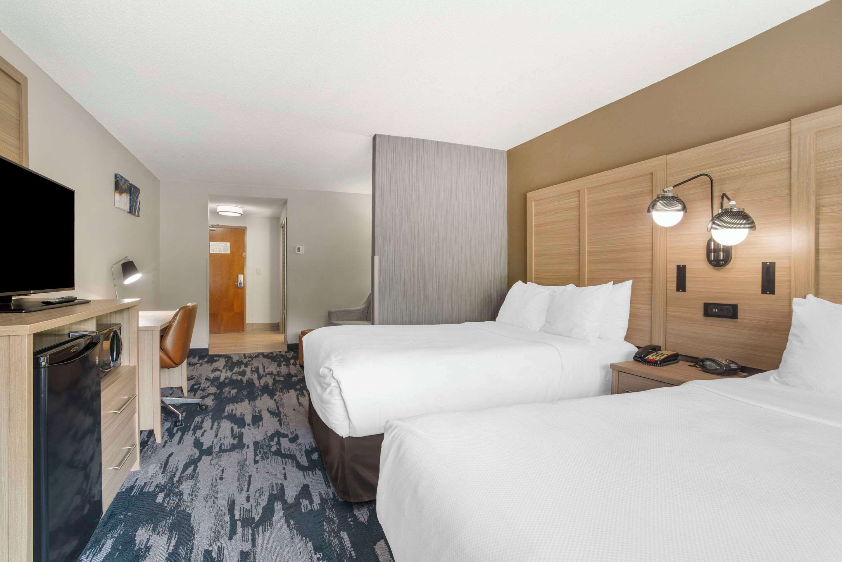A hotel room with two beds, a desk, a TV, and a bathroom.