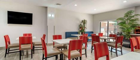 A modern dining area with red and beige chairs, white tables, and a flat-screen TV mounted on the wall.