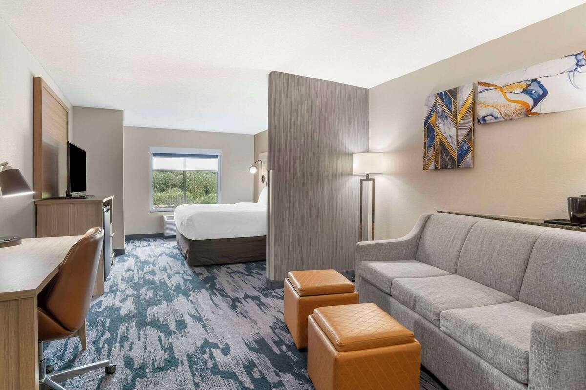 A hotel room with a bed, a desk, a sofa, and a window with a view of greenery.