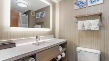 A modern bathroom with a large mirror, a sink, a toilet, and towel racks.
