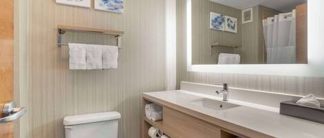 A modern bathroom with a toilet, sink, and mirror. There are towels on the wall and shelves.