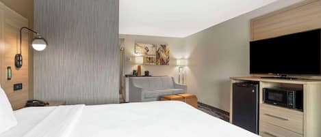 A hotel room with a bed, a grey sofa, a TV, a microwave, and a small table.