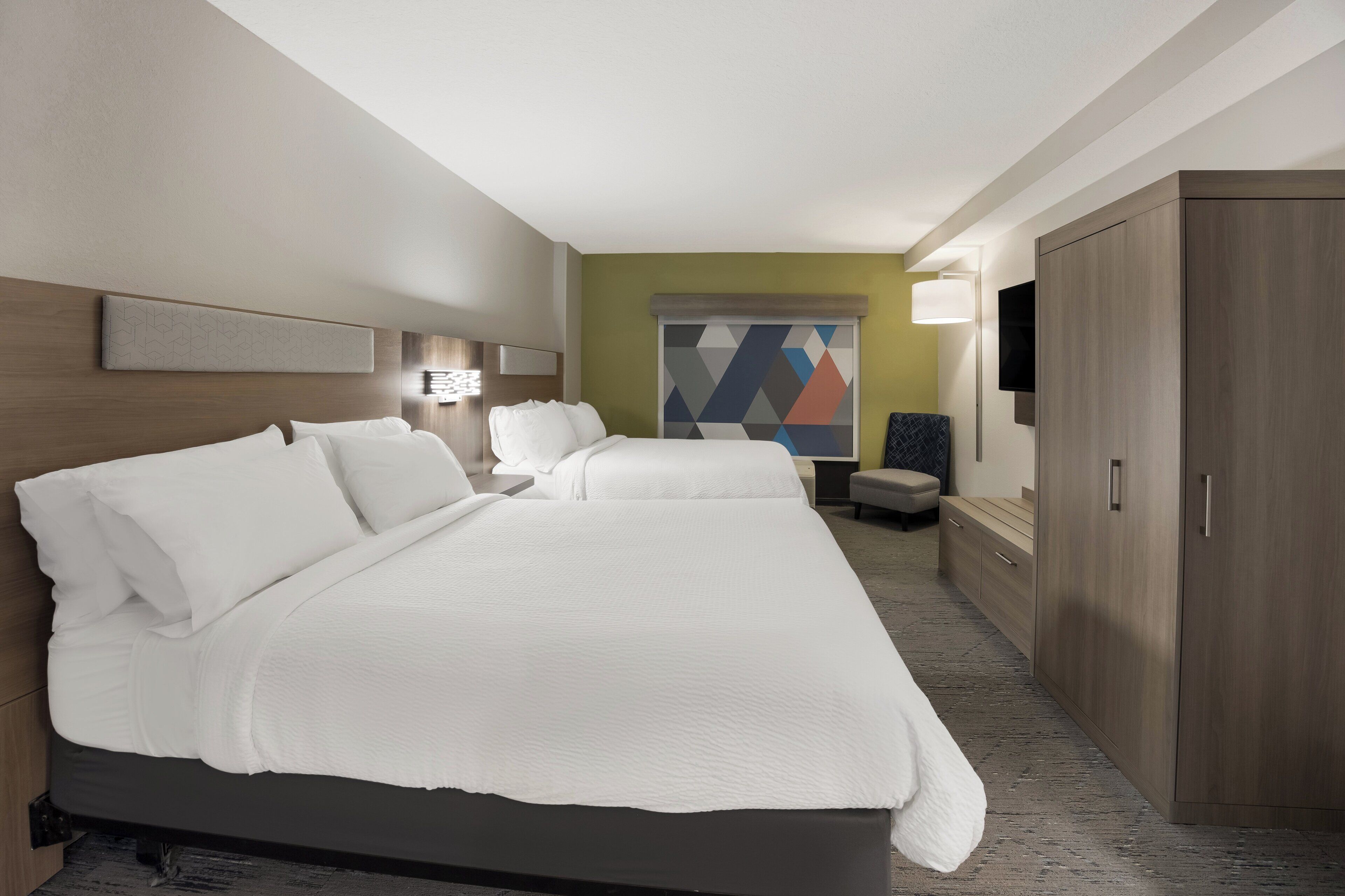 Ein Hotelzimmer mit einem großen Bett, einem Schreibtisch, einem Sessel, einem Kleiderschrank und einem Fernseher.
