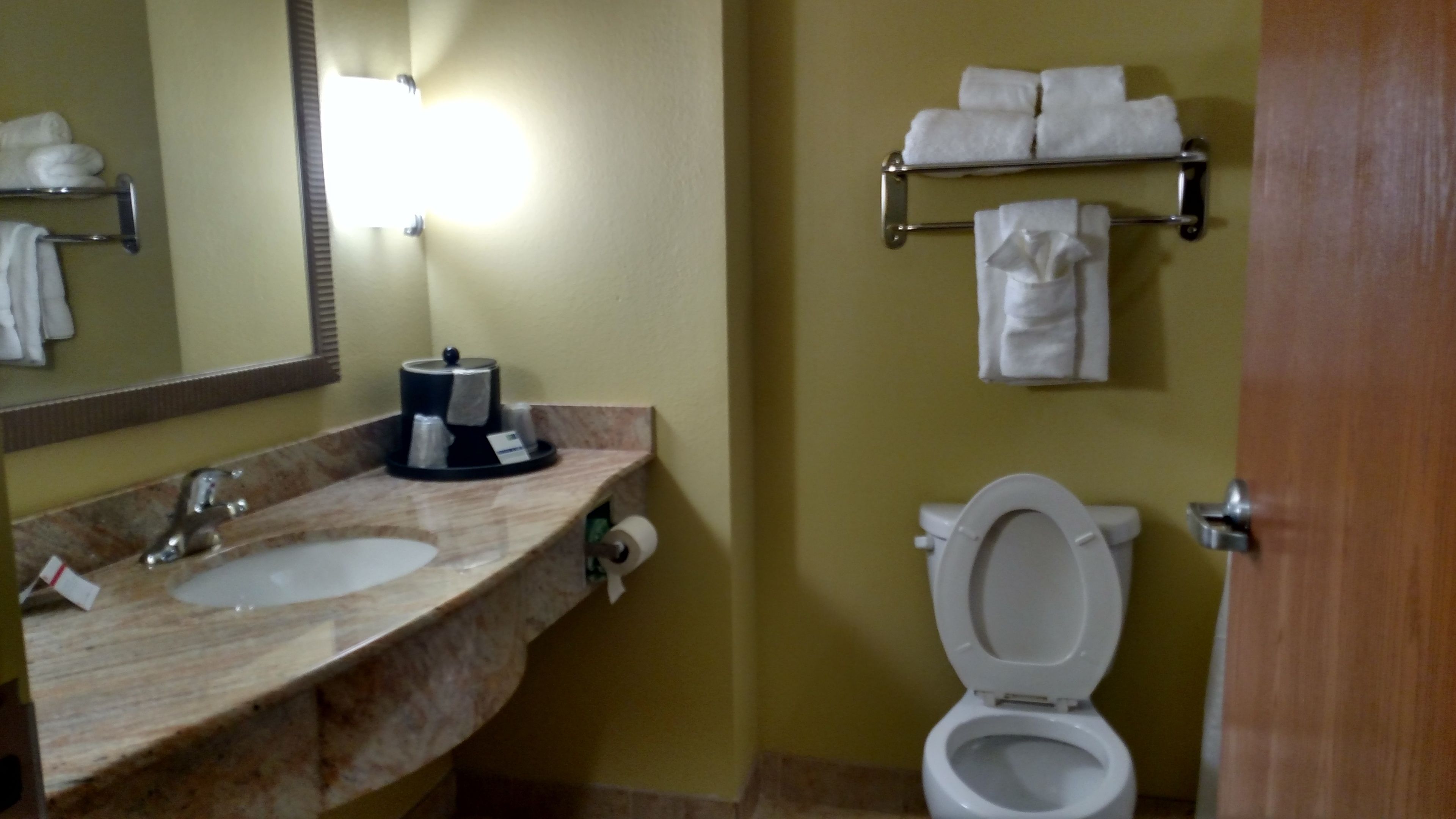 Un baño con lavamanos, espejo, toallero y retrete.