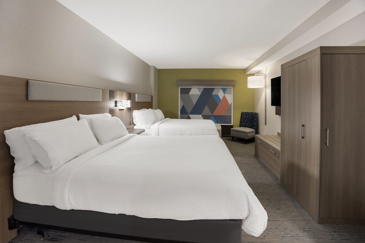 A hotel room with a large bed, a desk, a chair, a TV, and a wardrobe.