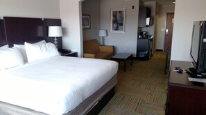Una habitación de hotel con una cama grande, un escritorio, una silla, un televisor y una kitchenette.
