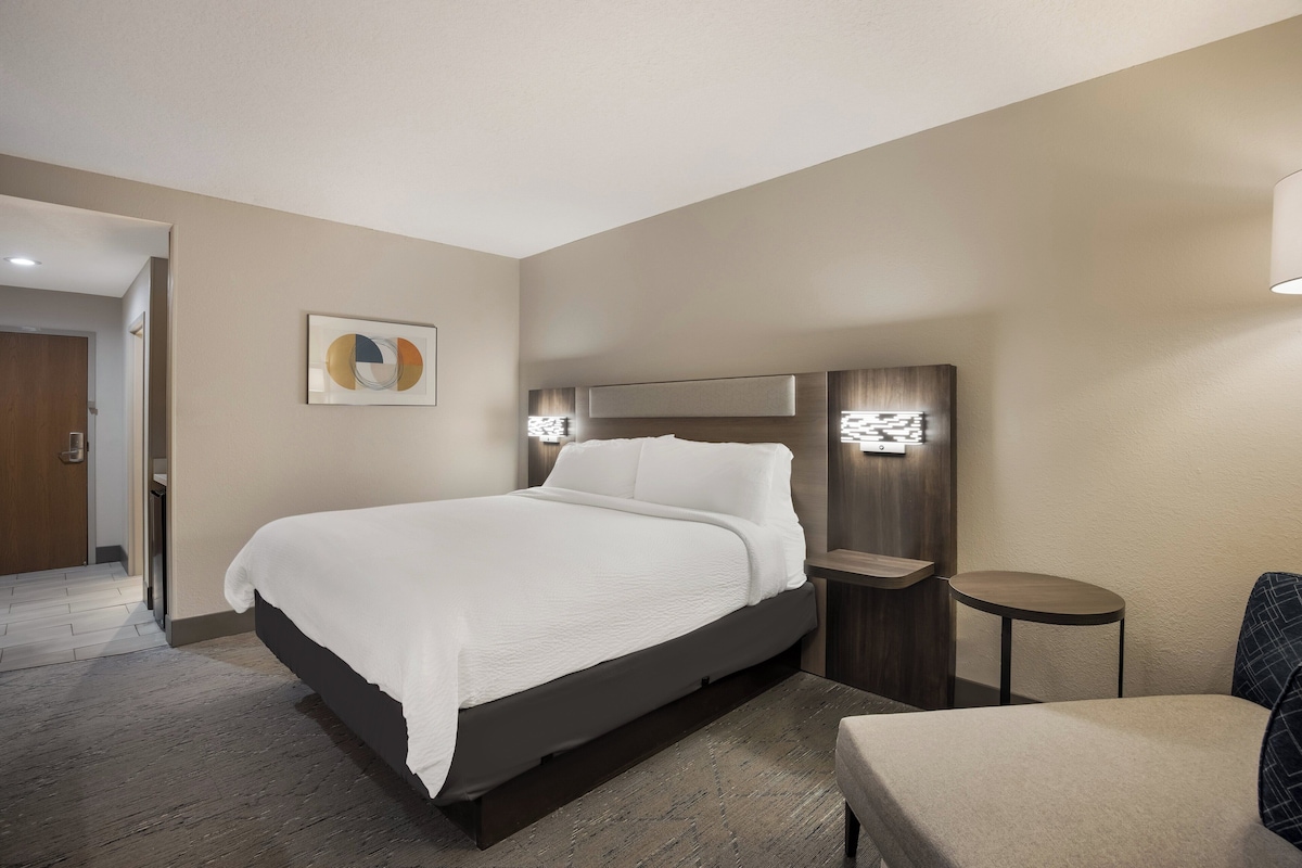 Une chambre d’hôtel avec un grand lit, une table de chevet, une chaise et un luminaire fixé au mur.