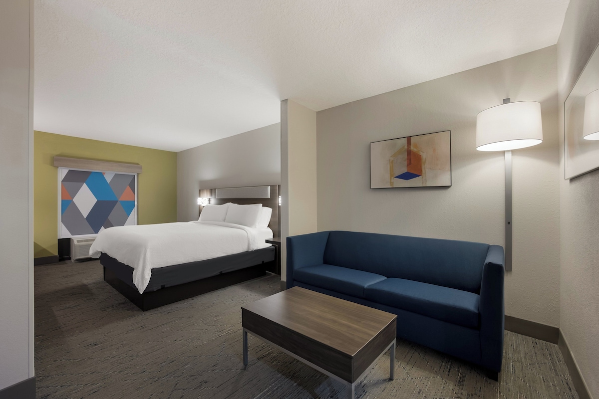 Une chambre d’hôtel avec un lit, un canapé bleu, une table basse en bois et un tableau au mur.