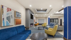 A modern hotel lobby with a blue sofa, yellow armchairs, a grey sofa, and a fireplace. - Holiday Inn Express Hotel & Suites PERRY by IHG (Perry)