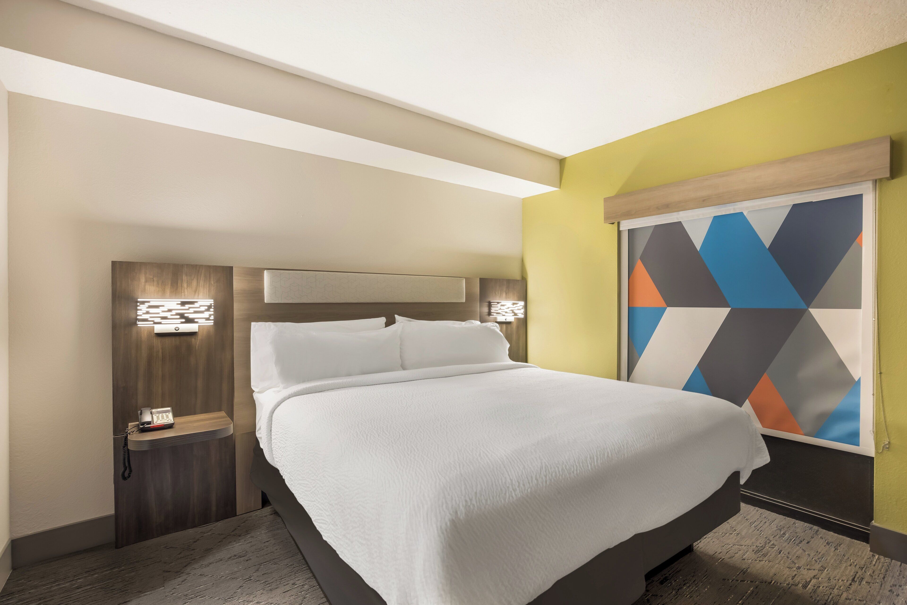 Ein Hotelzimmer mit einem Bett, Nachttischen, einer Wandlampe und einem Wandbild mit geometrischem Muster.