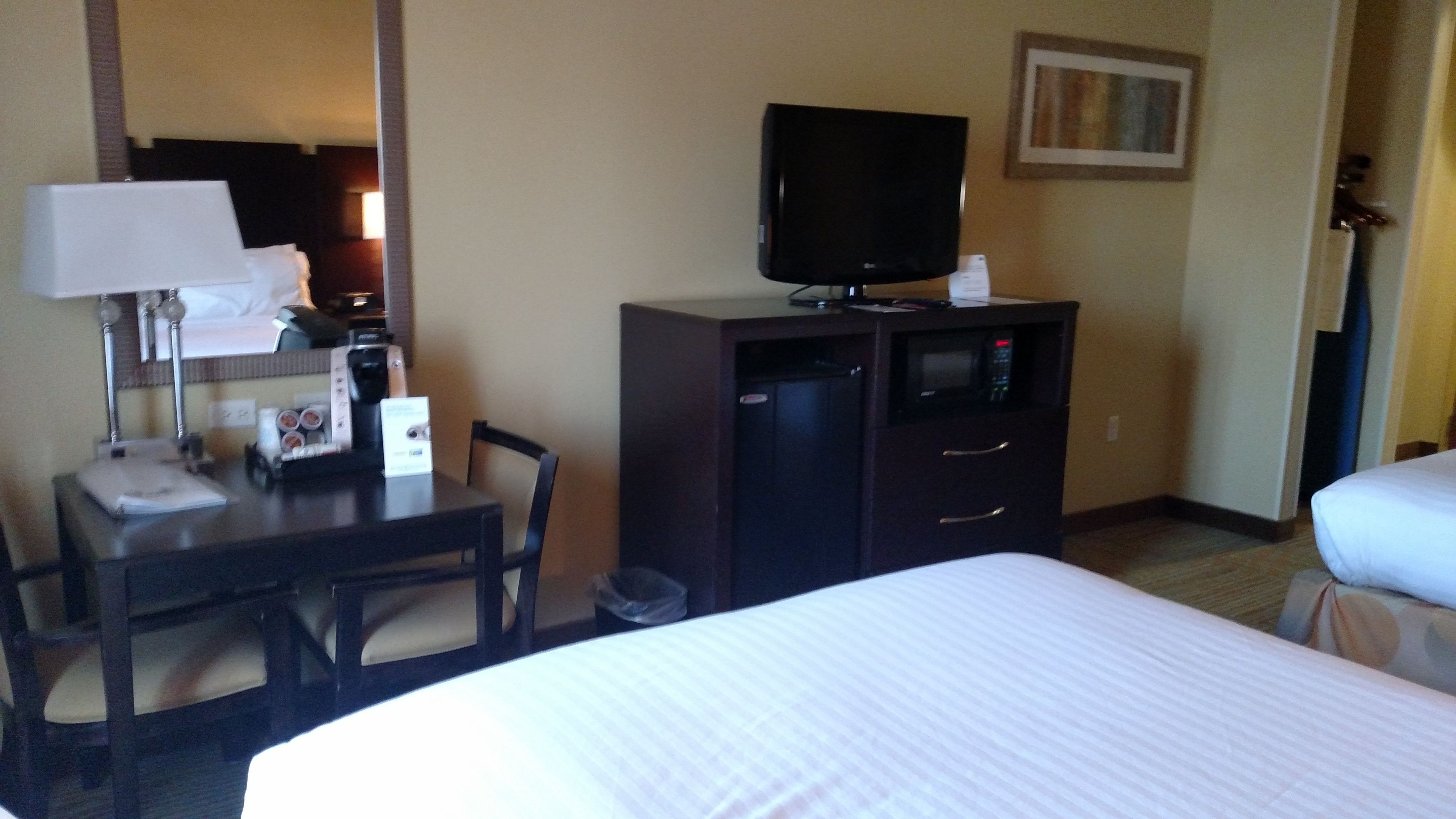 Une chambre d’hôtel comprenant un lit, un bureau avec une lampe, une télévision, un four à micro-ondes et une chaise.