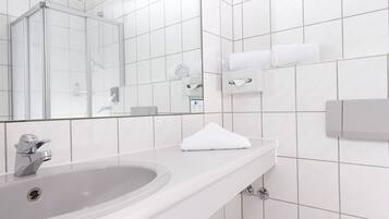 Ein modernes Badezimmer mit einem weißen Waschbecken, einer Glasdusche, einem Spiegel und einem Handtuchspender.