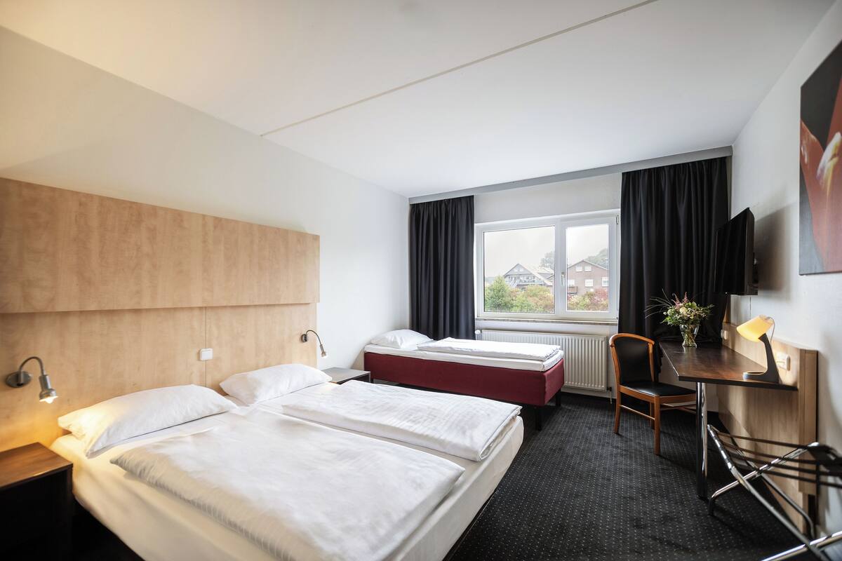 A hotel room with two beds, a desk with a chair, a TV, and a window with curtains.