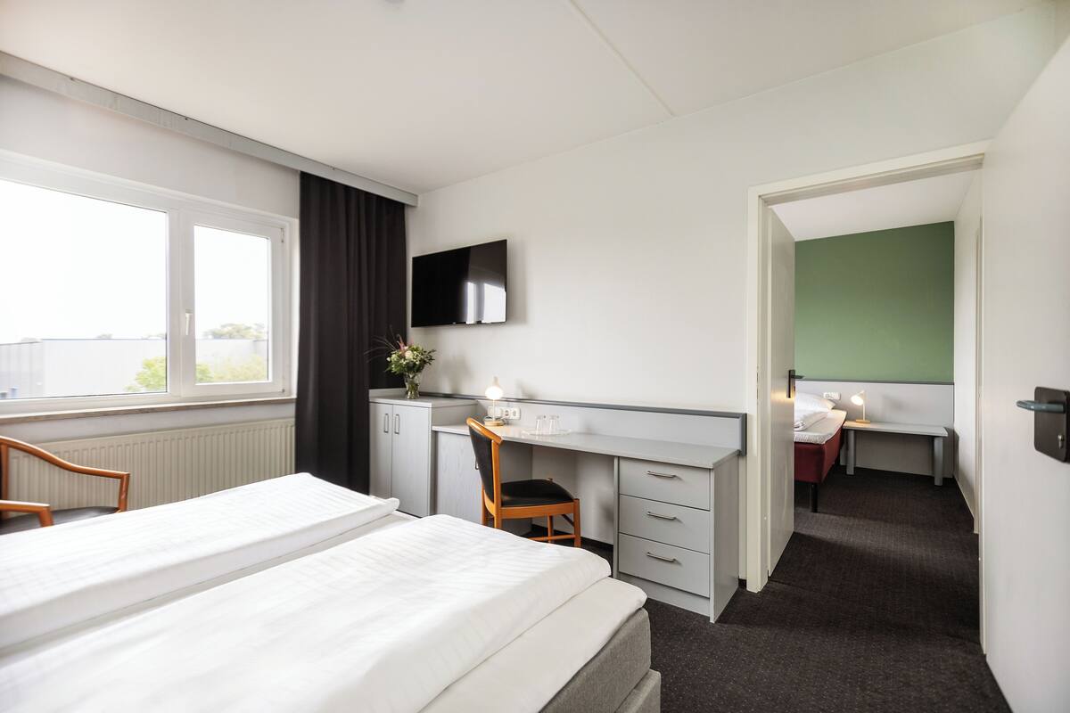 A hotel room with a bed, a desk, a chair, a TV, and a bathroom.