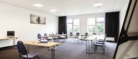 A conference room with a long table, chairs, a projector, and a large window with curtains.