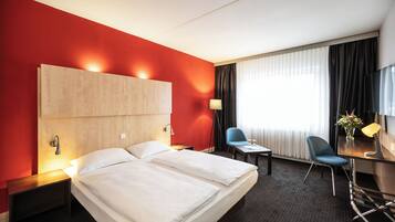 Een hotelkamer met een groot bed, een bureau met stoel, een lamp en een raam met gordijnen.