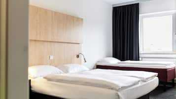 A hotel room with two beds, a wooden headboard, a window with black curtains, and a white wall.