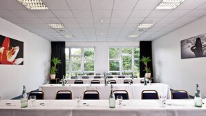 Sala de conferências com várias mesas, cadeiras e amplas janelas que oferecem vista para o verde lá fora.