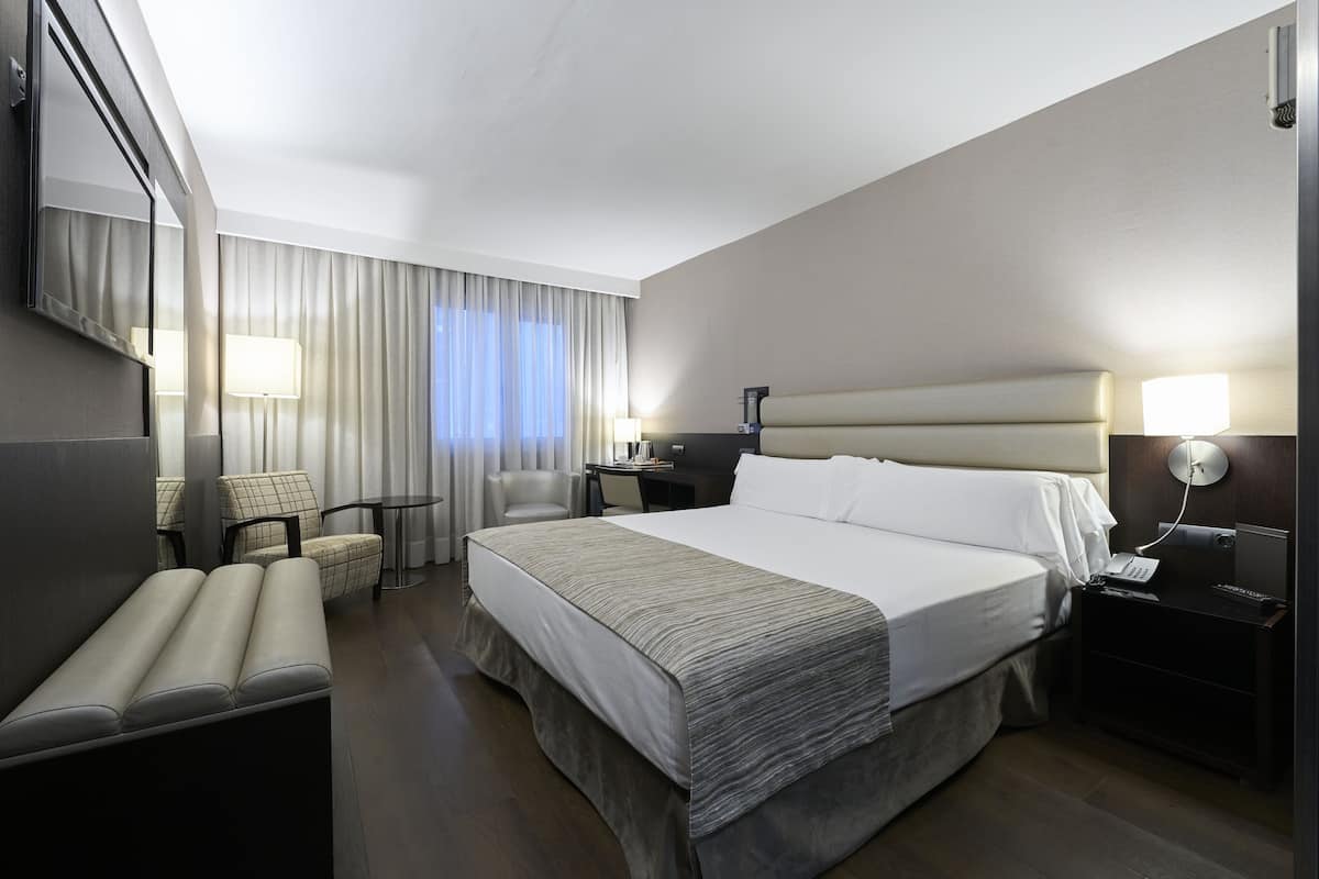 Une chambre d’hôtel moderne avec un grand lit, des tables de chevet, un bureau, une chaise et un banc.