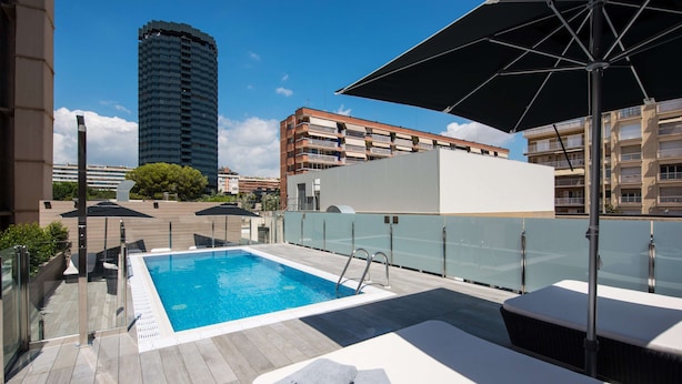 Un área de piscina en la azotea con vistas despejadas al horizonte de la ciudad, incluyendo un edificio alto y edificios residenciales.
