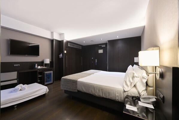 A modern hotel room with a large bed, bedside table with a lamp, a TV mounted on the wall, and a small desk with a computer. - Catalonia Rigoletto Hotel (Barcelona)