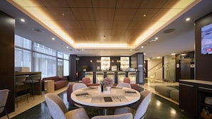Un lobby moderno de hotel con una mesa redonda para comer, asientos cómodos, una zona de bar y una escalera que conduce a un piso superior.