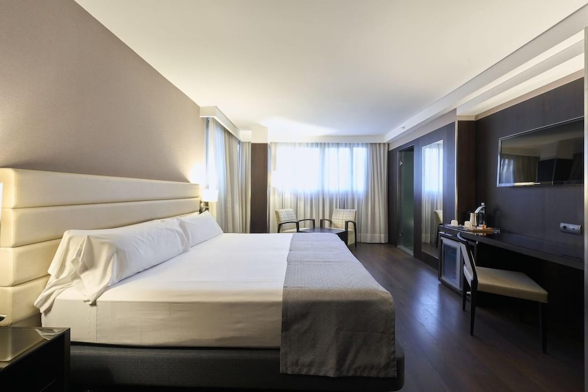 Una habitación de hotel con una cama grande, un escritorio, una silla y un televisor.