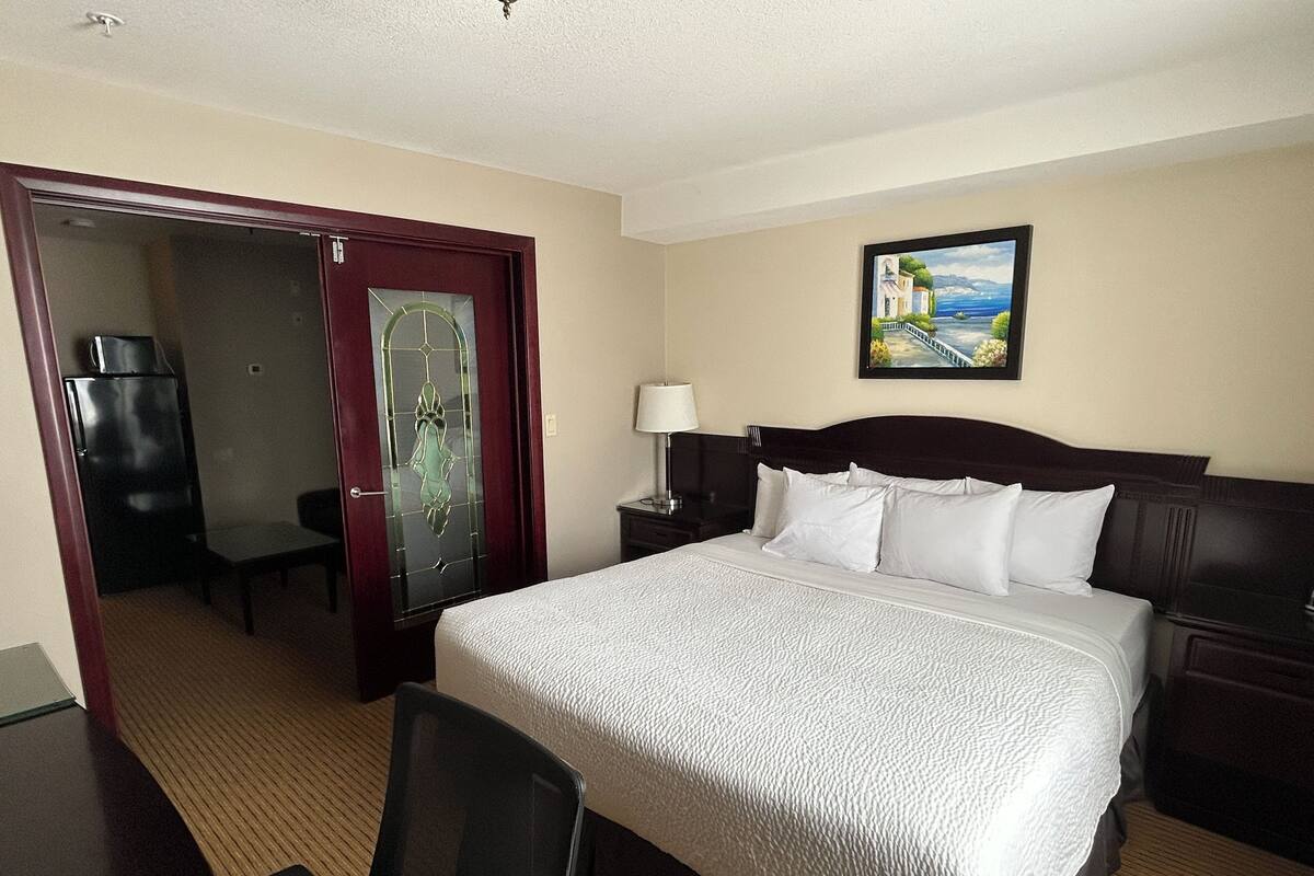 A hotel room with a bed, a desk, a chair, a door, and a painting on the wall.