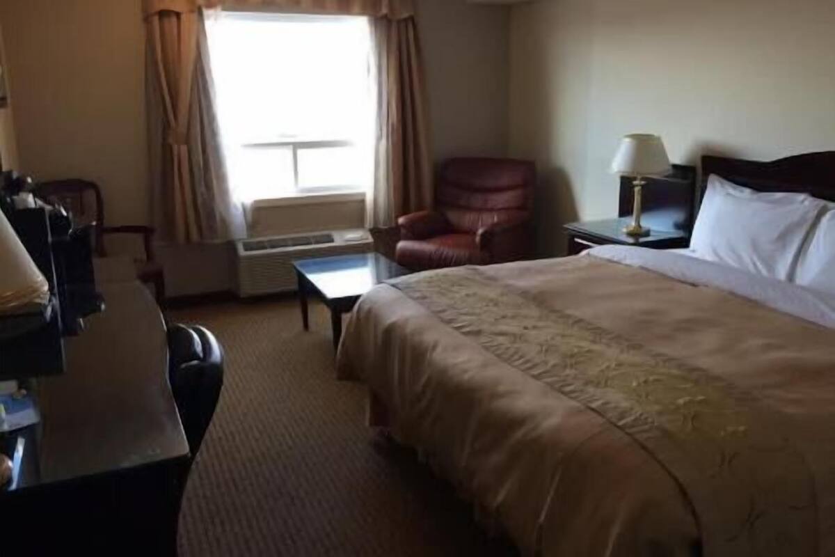 A hotel room with a bed, a desk, a chair, a lamp, and a window with curtains.
