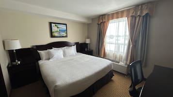 Habitación de hotel con cama, escritorio, silla, lámpara, un cuadro en la pared y una ventana con cortinas.