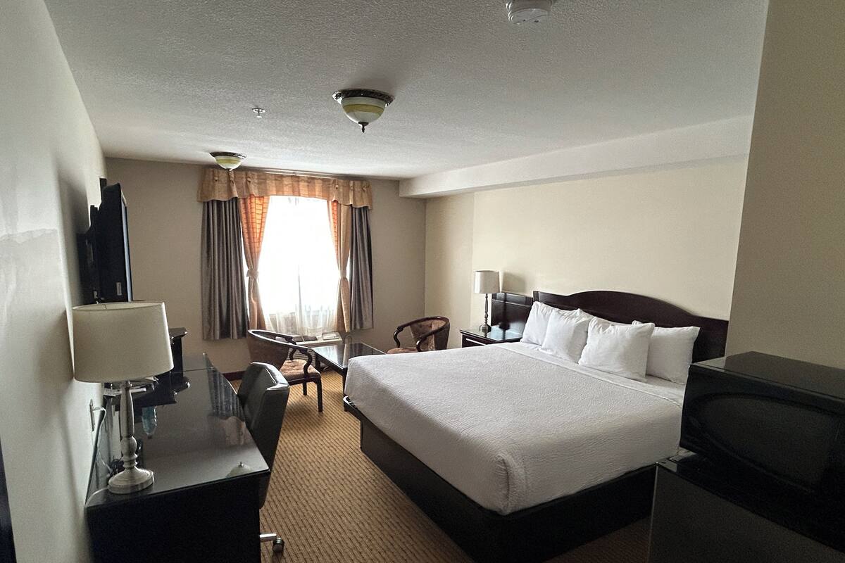 A hotel room with a bed, desk, chair, television, and a window with curtains.