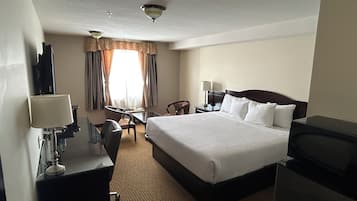Una habitación de hotel con cama, escritorio, silla, televisor y ventana con cortinas.
