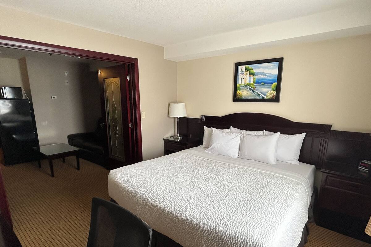 A hotel room with a bed, a desk, a chair, a wardrobe, and a painting on the wall.