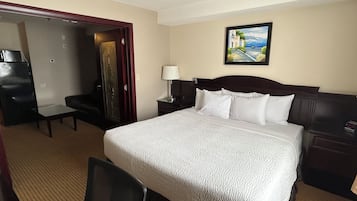 A hotel room with a bed, a desk, a chair, a wardrobe, and a painting on the wall.