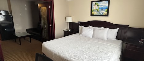 Habitación de hotel con cama, escritorio, silla, armario y un cuadro en la pared.