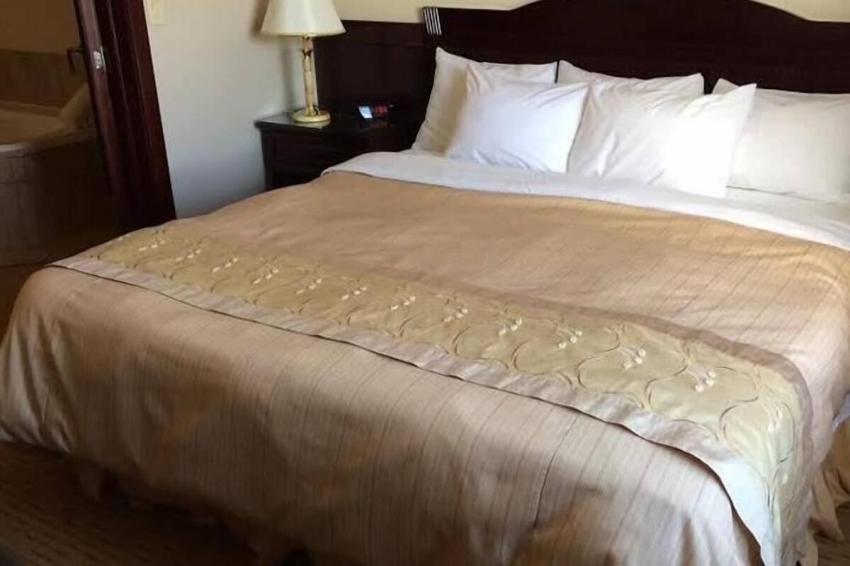 A neatly made bed with a beige bedspread and pillows, a wooden headboard, and a nightstand with a lamp.