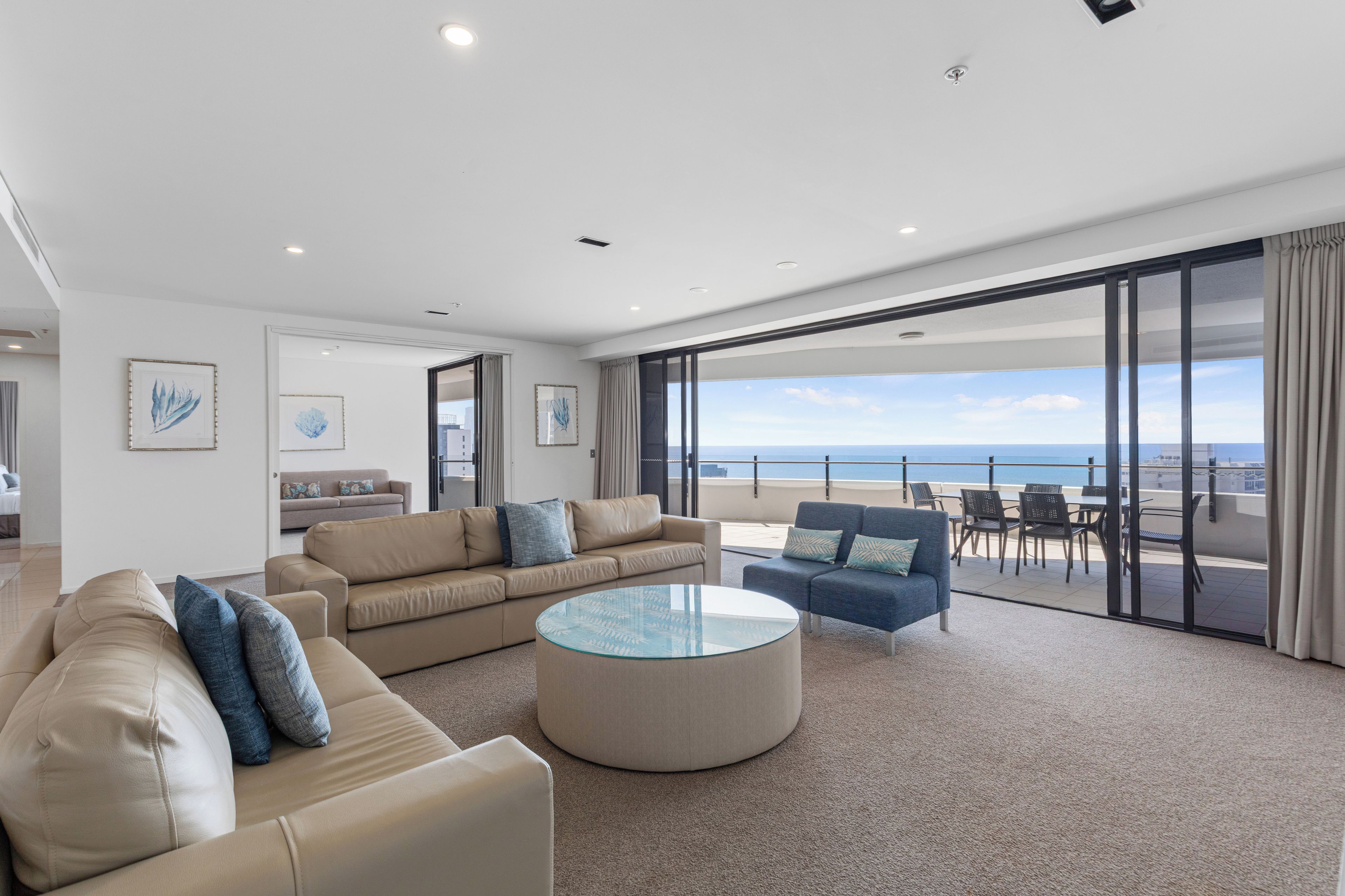 Ein modernes Wohnzimmer mit einem großen Glastisch, Sofas und Meerblick.