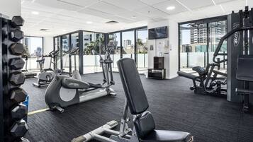 Uma academia com equipamentos de cardio, aparelhos de musculação e uma ampla janela com vista para a cidade.