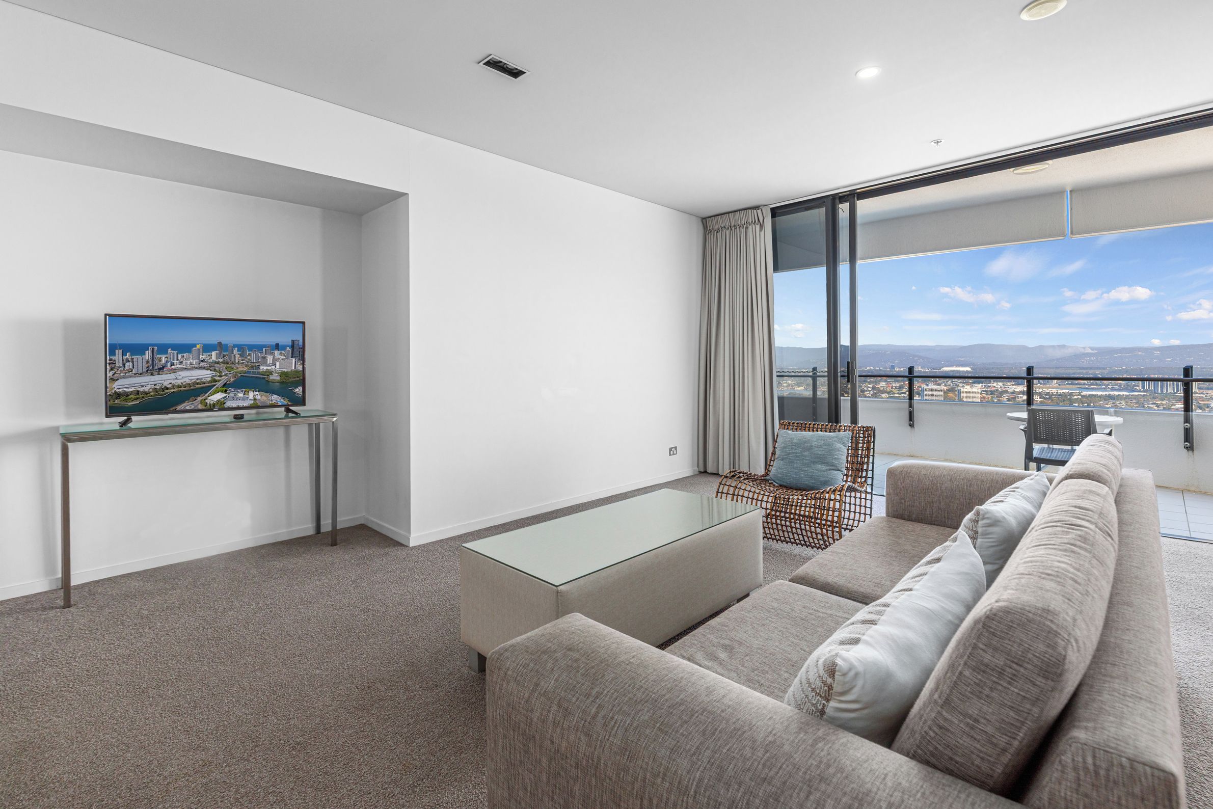 A modern living room with a glass coffee table, a sofa, and a television on a stand.