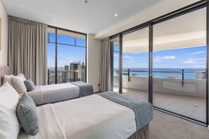 A hotel room with two beds, a large window, and a view of the city and sea.