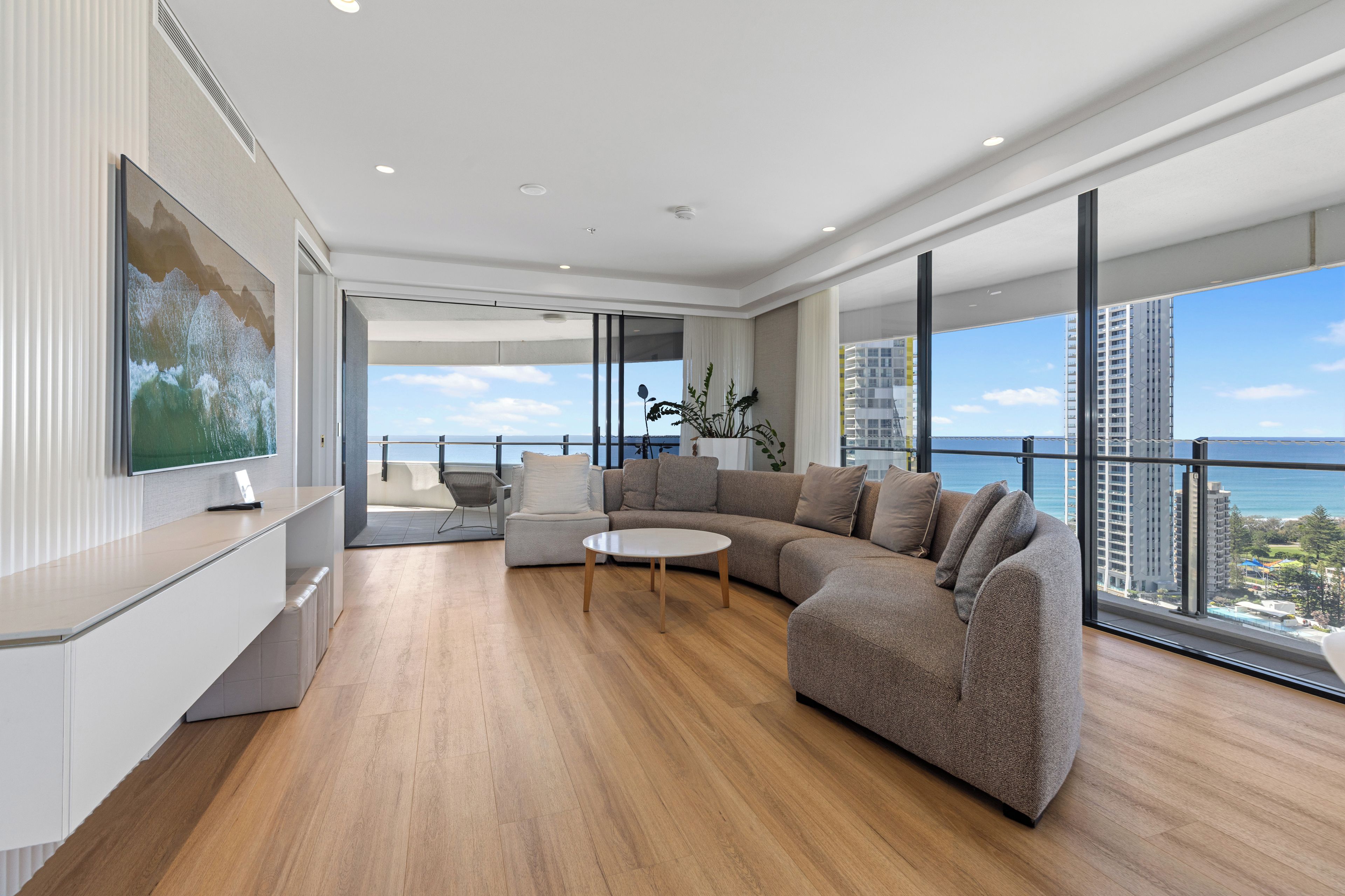A modern living room with a large sectional sofa, a coffee table, and a television on a wall.