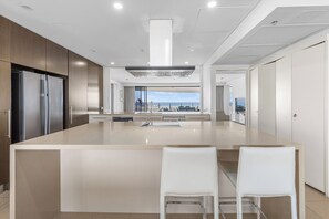 Een moderne keuken met een groot eiland, roestvrijstalen apparatuur en uitzicht op zee.
