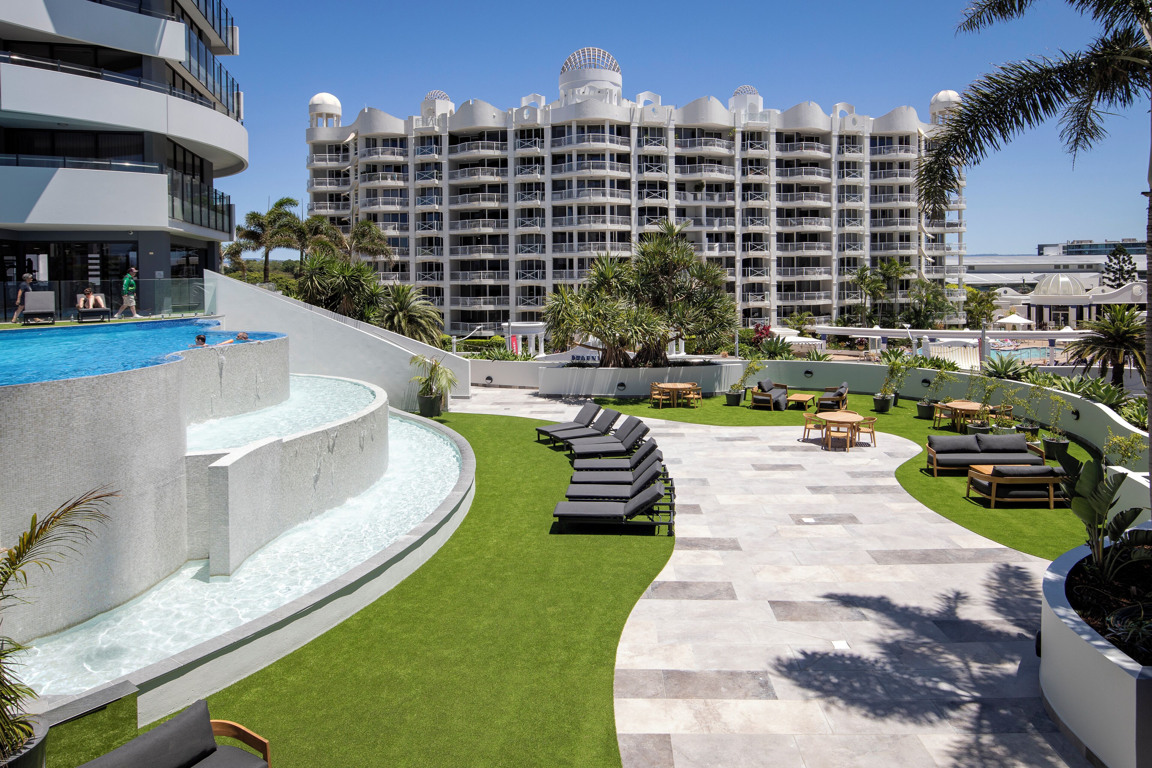 A resort with a swimming pool, lounge chairs, and a large building in the background.