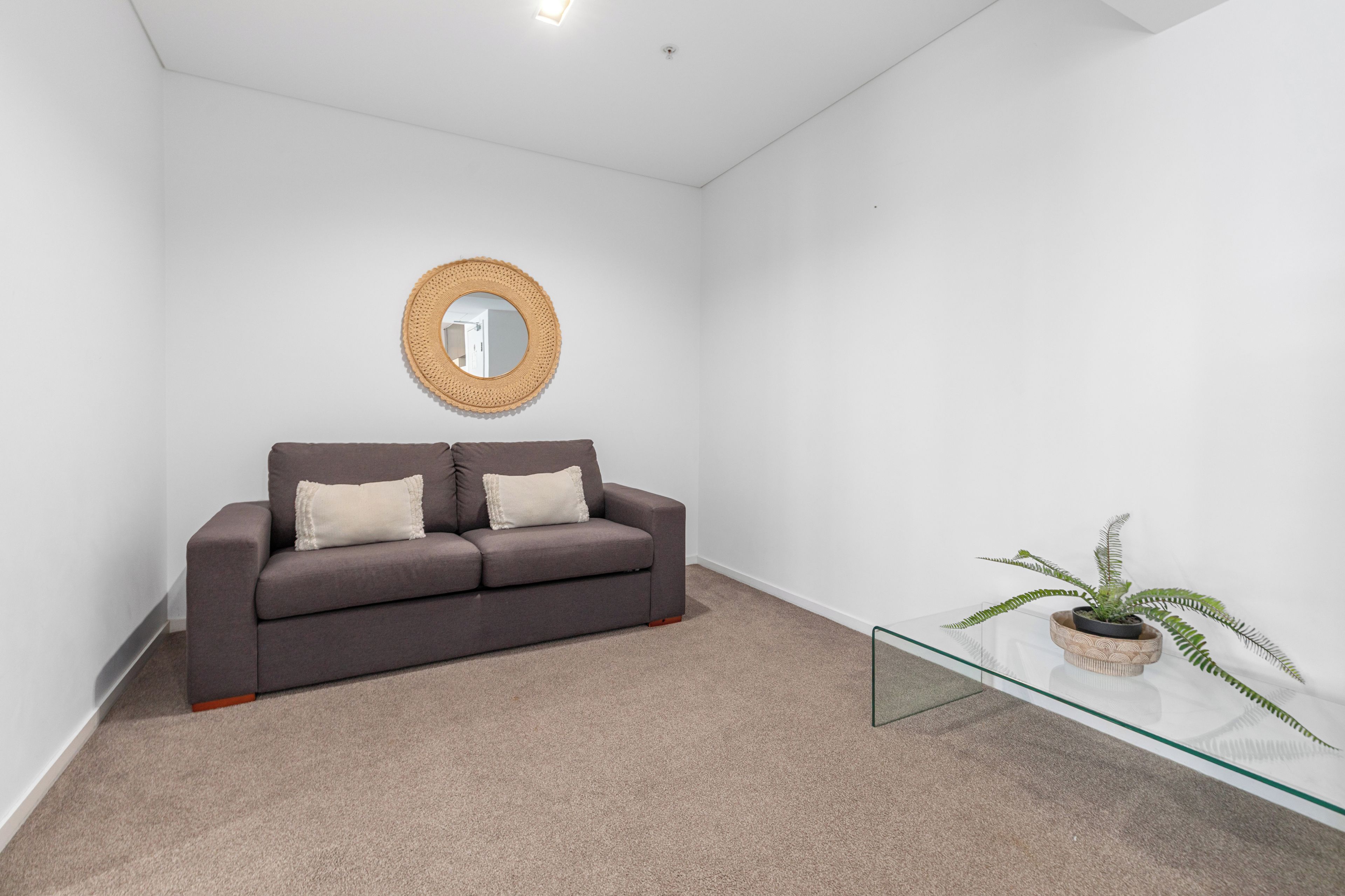 A room with a grey sofa, a round mirror, and a glass coffee table with a plant.