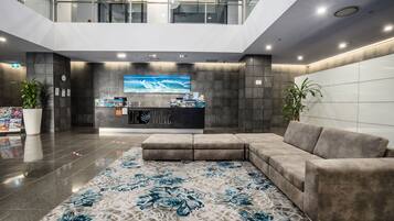 Um lobby moderno com balcão de recepção, uma tela digital grande e uma área de estar confortável.