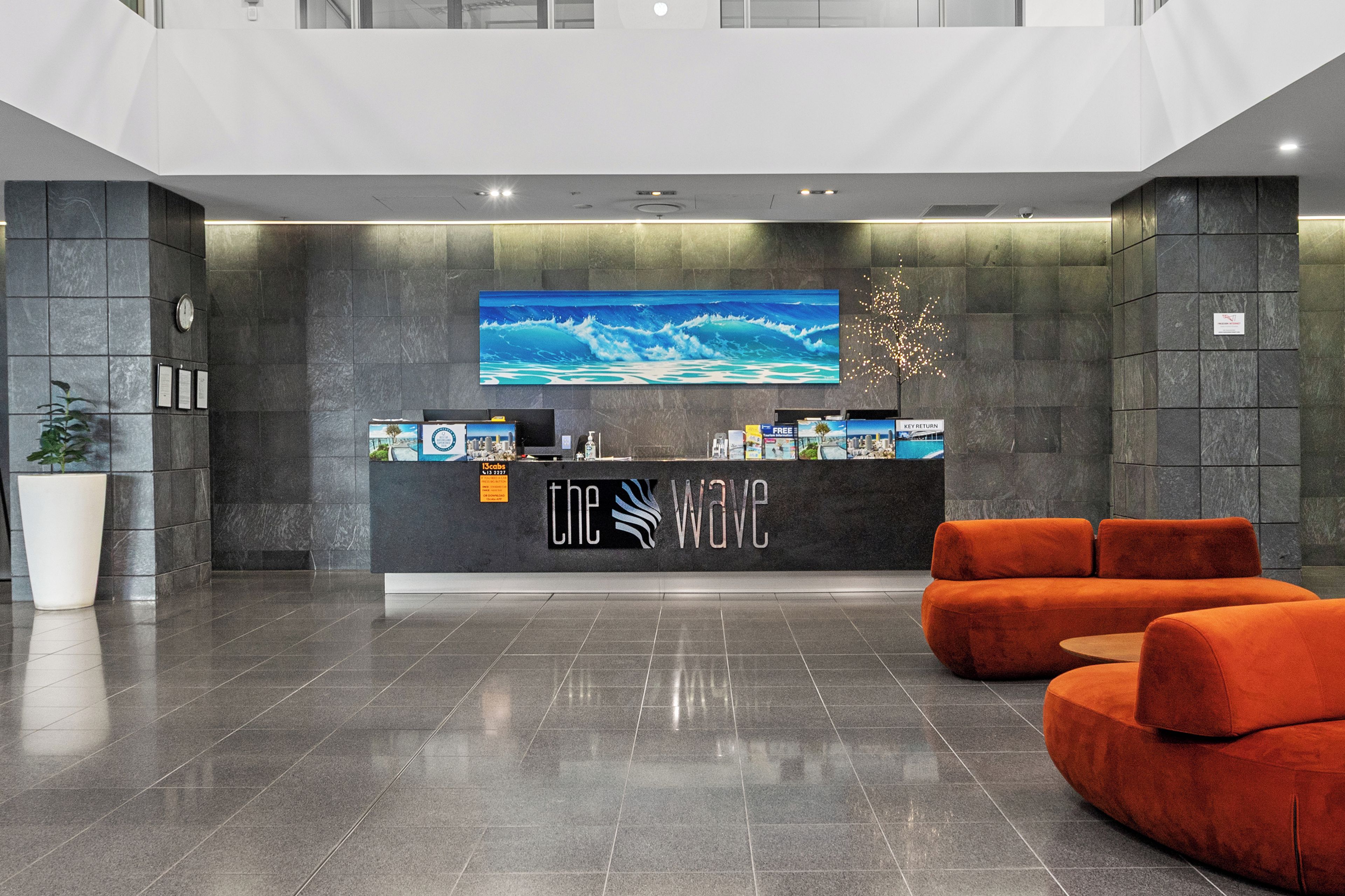 A reception desk with a large ocean wave painting, a 'Key Return' sign, and a '13cabs' sign.