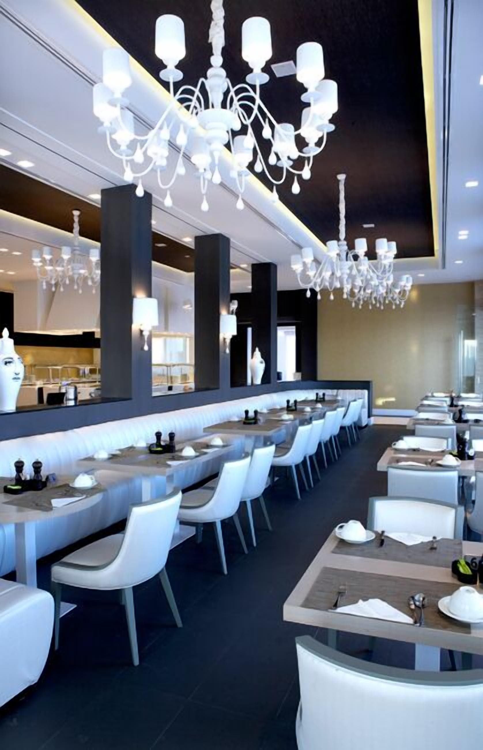 A modern restaurant with a long counter, white chairs, and a chandelier.