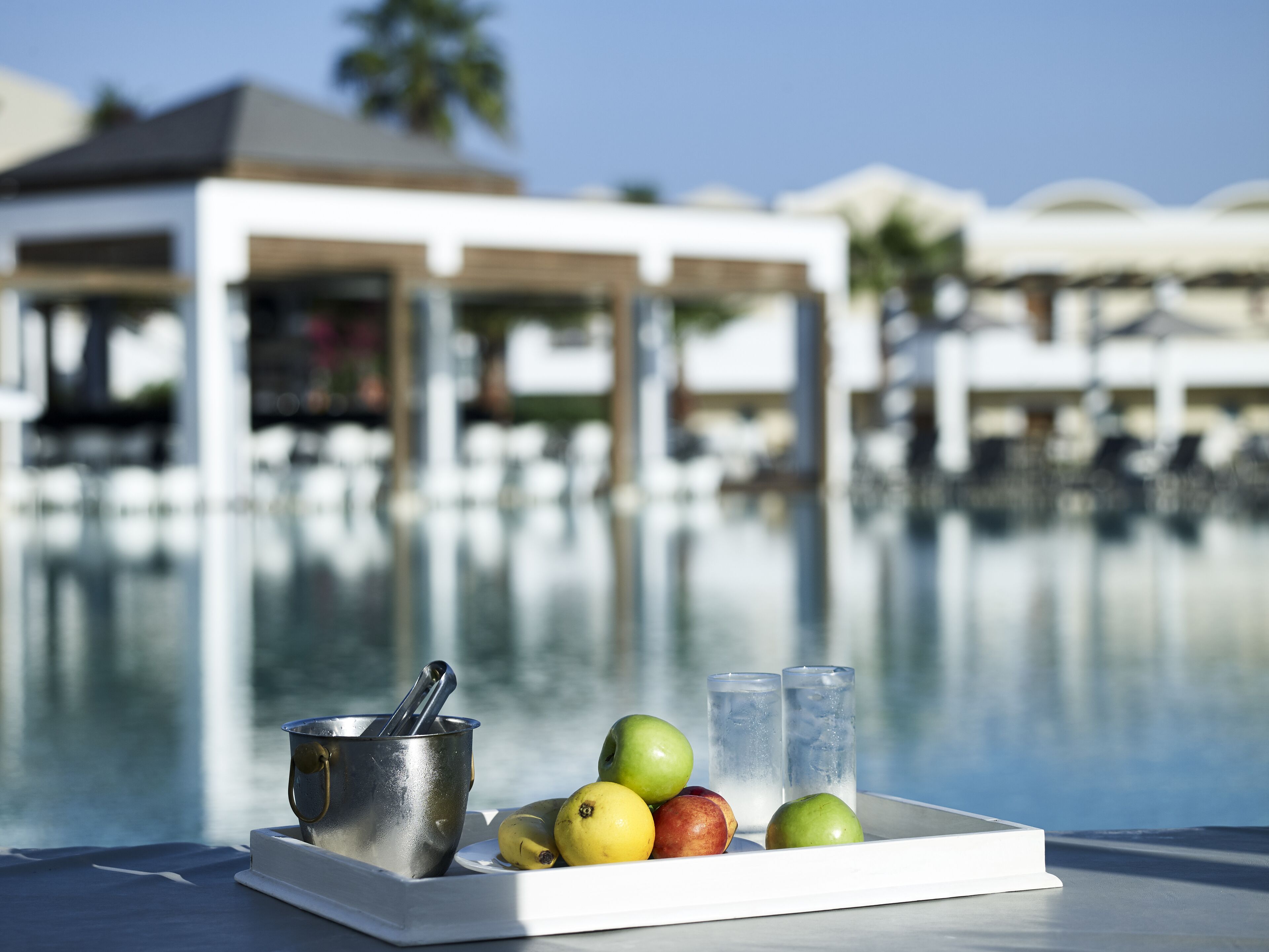 Una bandeja con frutas y un recipiente metálico junto a una piscina.