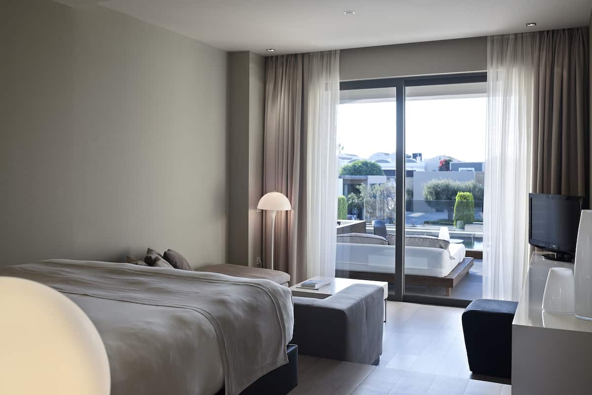 A modern hotel room with a large bed, a desk, a TV, and a view of the city.